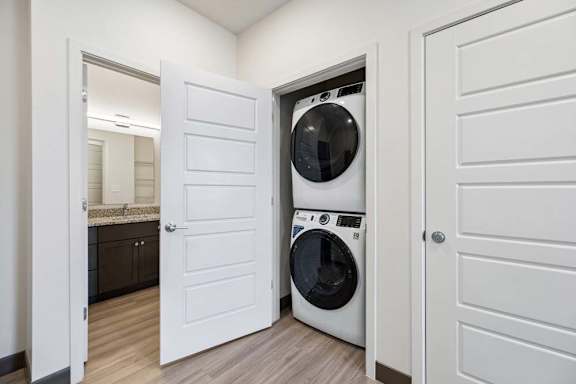 In-unit laundry area with a stacked washer and dryer positioned between the bathroom and storage closet.