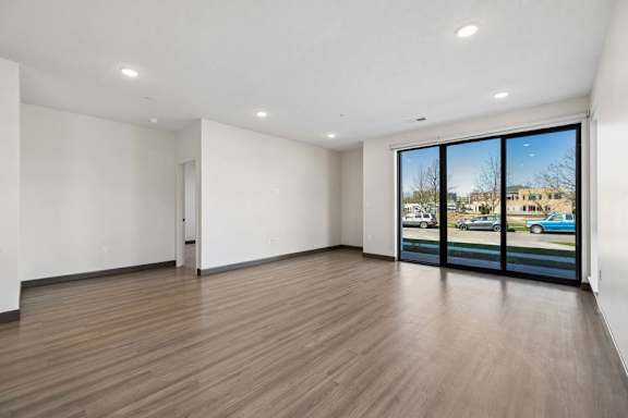Spacious living area with wood-style flooring and floor-to-ceiling glass doors overlooking the street.