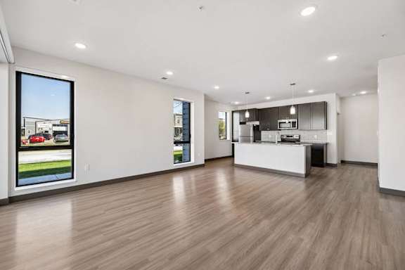 Expansive living space with wood-style flooring, tall windows, and an open kitchen with island seating.