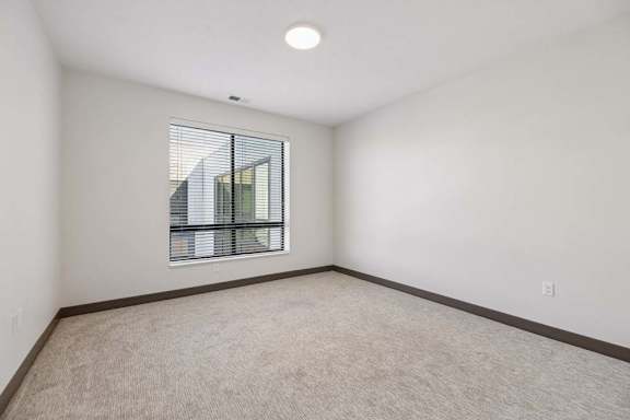 Unfurnished bedroom with neutral carpeting, white walls, dark trim, and a large window with horizontal blinds.