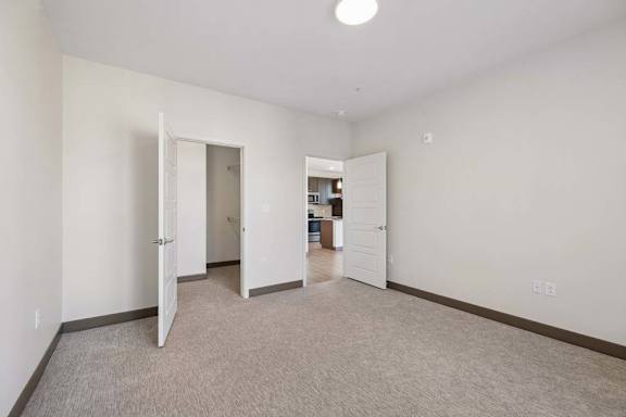 Carpeted bedroom with an open closet and doorway leading toward the kitchen and main living area.