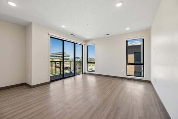 Open living area with wood-style flooring, expansive windows, and sliding glass doors leading to a private balcony.