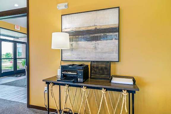 A clubhouse office space featuring a table with a printer, a tray of paper, and a lamp on it.