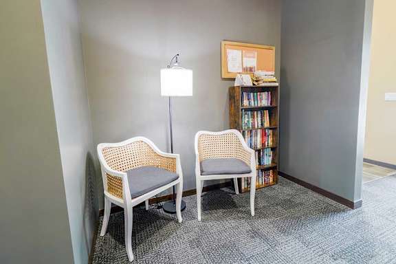 Two chairs are placed in a nook with a lamp and full bookshelf.