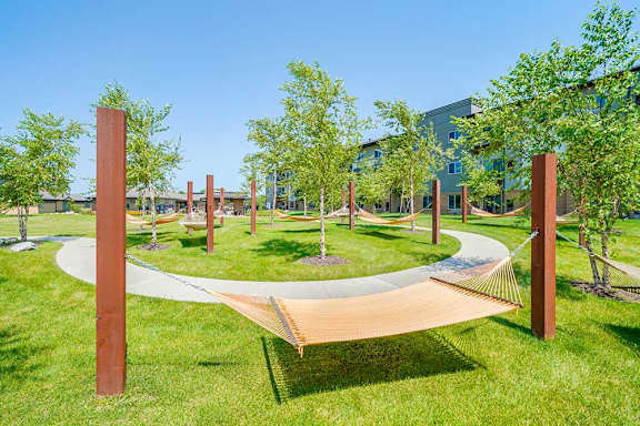 A hammock garden with several cloth-style hammocks, metal mounting posts, trees for shade, and a walking path that weaves between.