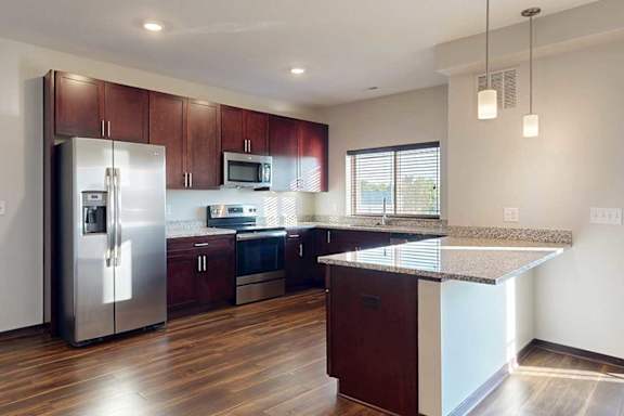 A modern kitchen with dark wooden cabinets, granite countertops, stainless steel appliances, a large window over the sink, and a peninsula counter.