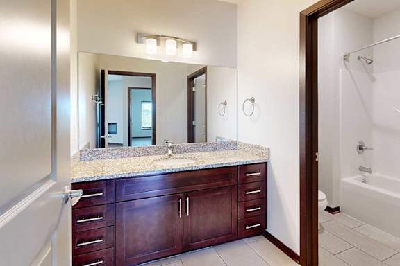 A bathroom with a granite vanity sink and a partitioned off shower room.