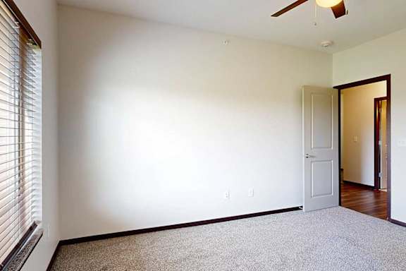 A bedroom with a ceiling fan and large window for added natural light.