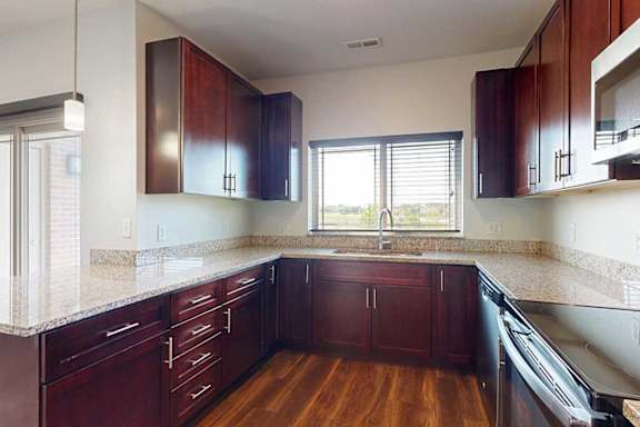 A modern kitchen with dark wooden cabinets, granite countertops, stainless steel appliances, a large window over the sink, and a peninsula counter.