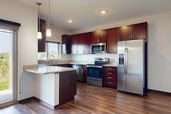 A modern kitchen with dark wooden cabinets, granite countertops, stainless steel appliances, a large window over the sink, and a peninsula counter.