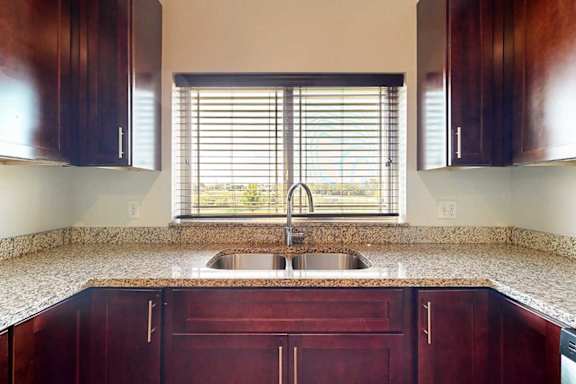 A kitchen with a stainless steel sink, granite counters, and a window above the sink.