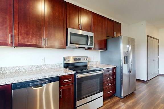 A modern kitchen with dark wooden cabinets, granite countertops, and stainless steel appliances.