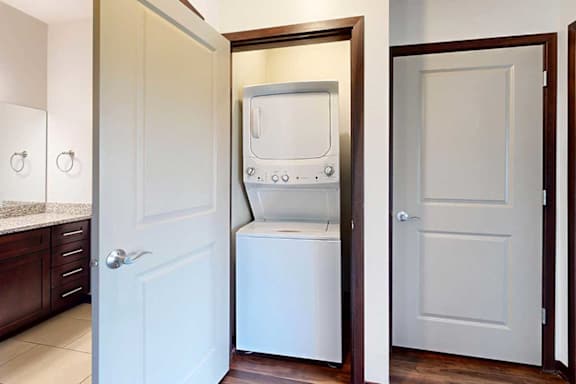 A stacked wash and dryer in a closet in the hallway next to the bathroom door.