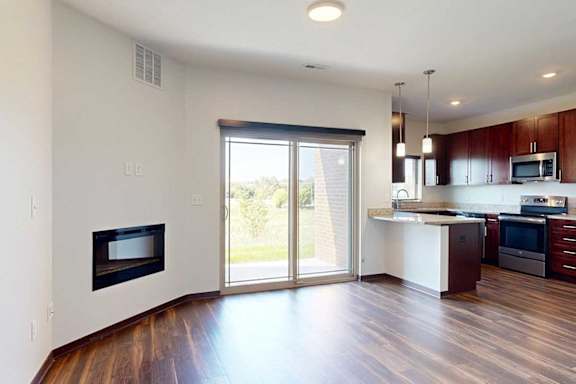 A living room with an electric fireplace, and a sliding glass door to a patio with a roller shade.