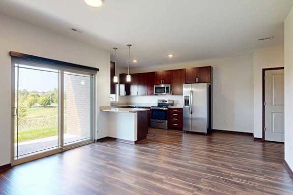 An open living room with sliding glass door to a patio, and modern kitchen with dark wooden cabinets.