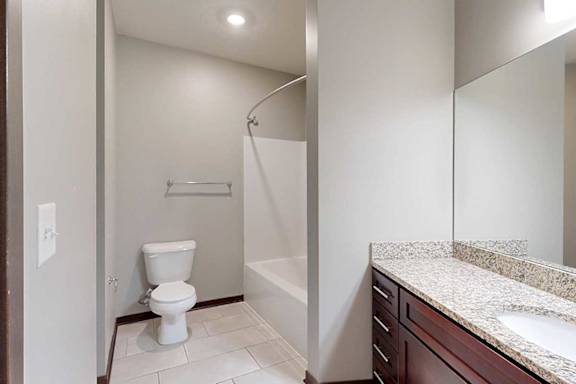 A long bathroom with a granite vanity sink, mirror, and tub shower.