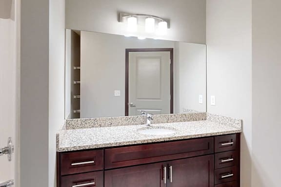 A bathroom with a granite vanity sink, an oversized mirror, and overhead lighting.