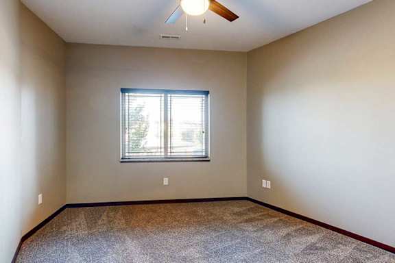 A carpeted bedroom with a large window and a ceiling fan.