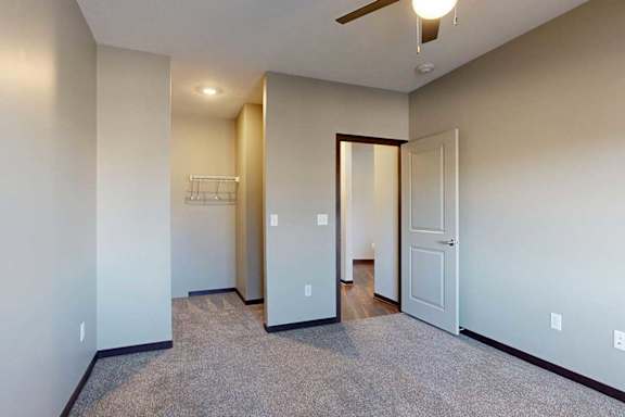 A carpeted bedroom with a ceiling fan and a spacious walk-in closet.