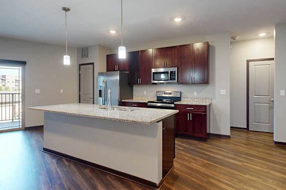 A modern kitchen with wooden cabinets, granite counters, a large central island, a pantry, and stainless steel appliances.