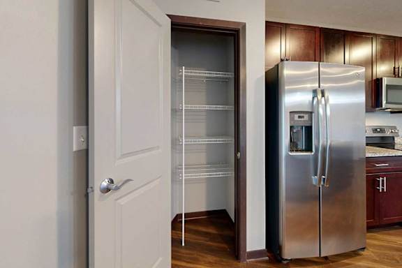 A kitchen pantry with built-in corner shelves next to a stainless steel fridge.