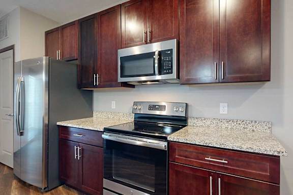 A close up on a kitchen with brown cabinets, granite counters, and stainless steel appliances.