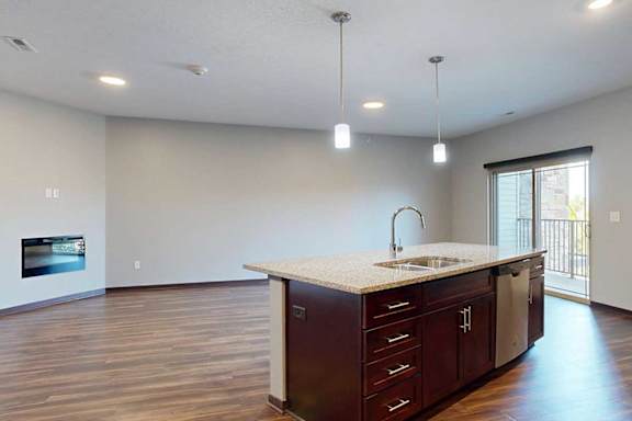 An open-concept living room with hardwood flooring and a sliding glass door to a balcony, that connects to a modern kitchen with a large central island.