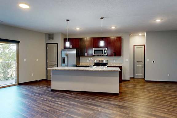 A modern kitchen with wooden cabinets, granite counters, a large central island, a pantry, and stainless steel appliances.