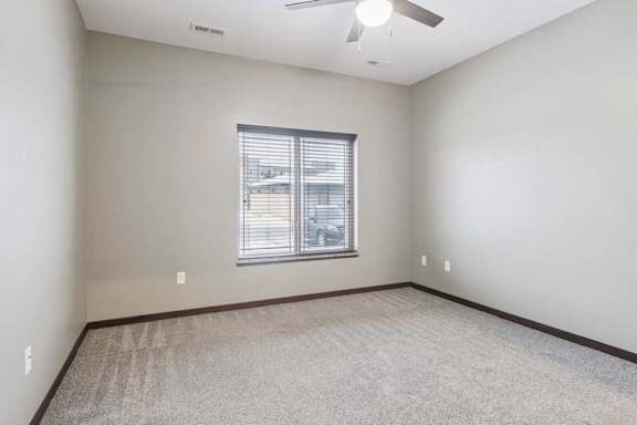 A carpeted bedroom with a ceiling fan and a window.
