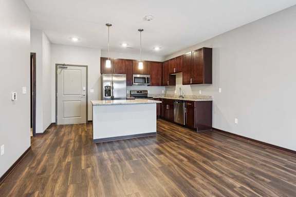 A living room with hardwood-style flooring and kitchen with dark wooden cabinets.