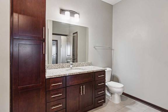 A bathroom with a granite vanity, dark wooden cabinets, and a large mirror with overhead lighting.