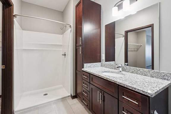 A bathroom with a granite vanity, dark wooden cabinets, and a walk-in shower.