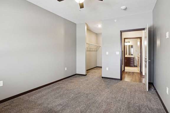 A carpeted bedroom with a ceiling fan and an open walk-in closet.