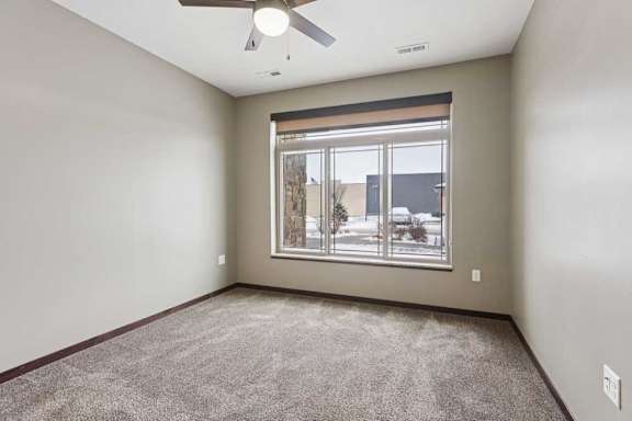 A carpeted bedroom with a ceiling fan and a floor-to-ceiling window.