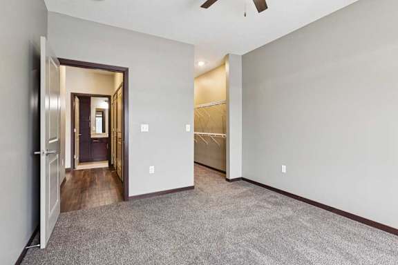 A carpeted bedroom with a ceiling fan and an open walk-in closet.