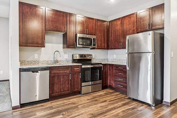 A kitchen with dark wood cabinets, granite countertops, and stainless steel appliances.