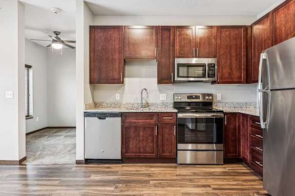 A kitchen with dark wood cabinets, granite countertops, and stainless steel appliances.