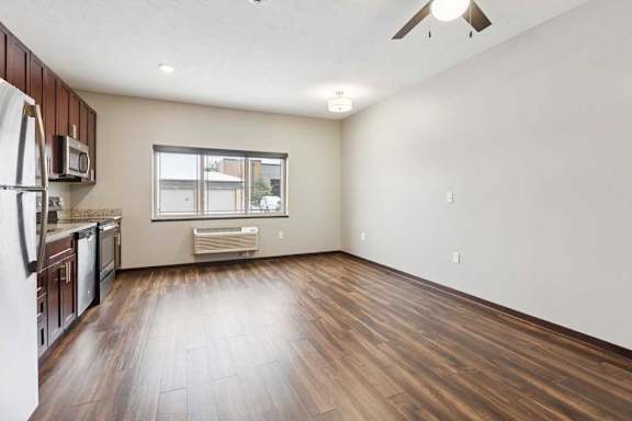 A living area with a ceiling fan, open to a kitchen with dark wooden cabinets.