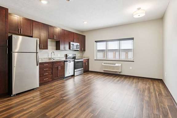 A living area with a three-panel window, open to a kitchen with dark wooden cabinets.