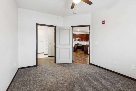 A carpeted bedroom with a ceiling fan and an open walk-in closet.