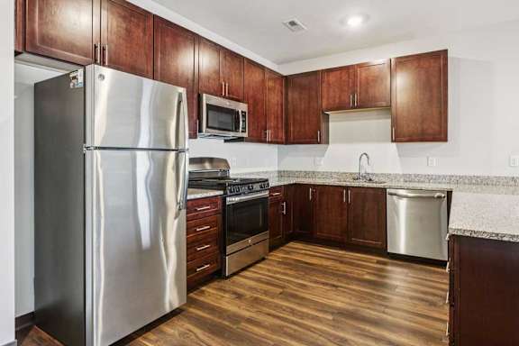 A kitchen with dark wood cabinets, granite countertops, and stainless steel appliances.
