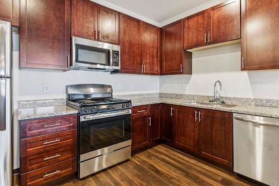 A kitchen with dark wood cabinets, granite countertops, and stainless steel appliances.