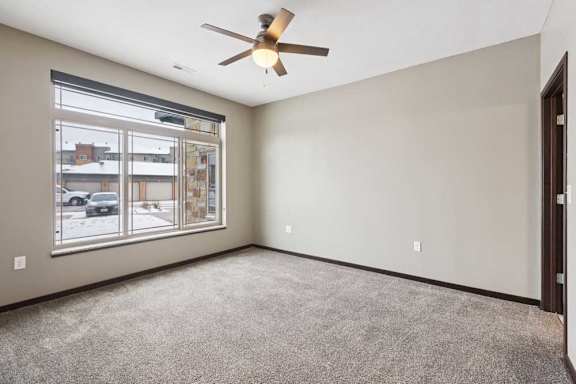 A carpeted bedroom with a ceiling fan and a floor-to-ceiling window.