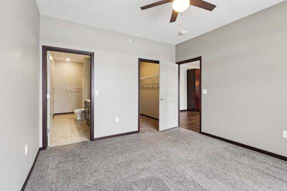 A carpeted bedroom with a ceiling fan, an attached bathroom, and an open walk-in closet.