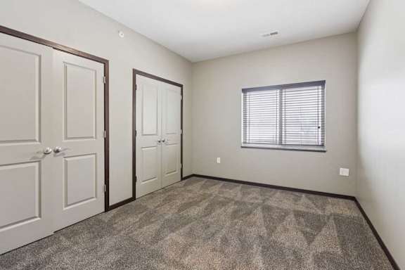 A carpeted bedroom with two double-door closets, and an oversized window.