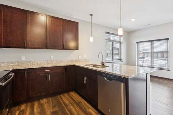 A kitchen with dark wood cabinets, granite countertops, stainless steel appliances, and a peninsula in front of a dining room..
