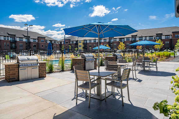 a patio with tables, chairs, and umbrellas with grills in the background