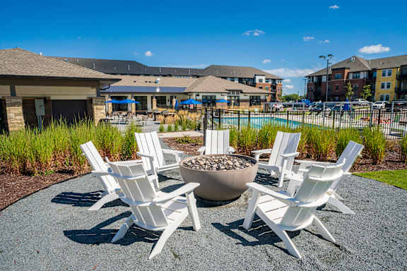 Four white chairs are arranged around a fire pit.
