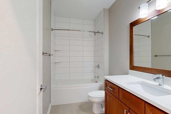A bathroom with cherry-stained wooden cabinets, white quartz vanity, and a tiled tub shower.