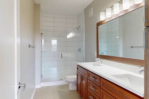 A bathroom with a cherry-stained wooden vanity with white quartz countertops, and a tiled walk-in shower with a glass door.